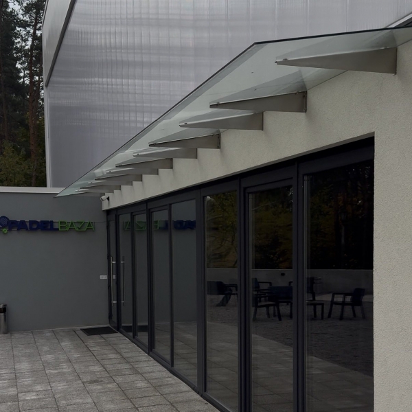 Стеклянный навес над входом в зал падел-корта из прозрачного стекла на кронштейнах — Trevi