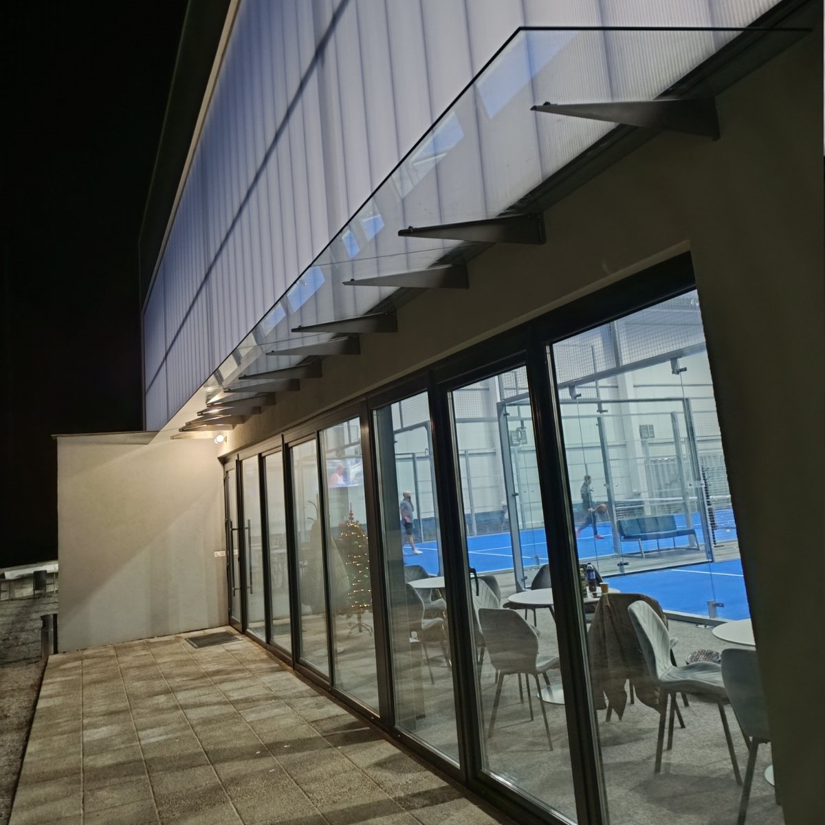 Стеклянный навес над входом в зал падел-корта из прозрачного стекла на кронштейнах — Trevi